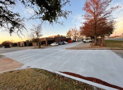 A street scene featuring a parking lot on one side and several trees lining the road, creating a pleasant urban environment.