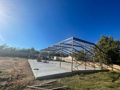 A partially built metal structure in a yard, surrounded by construction materials and tools.

