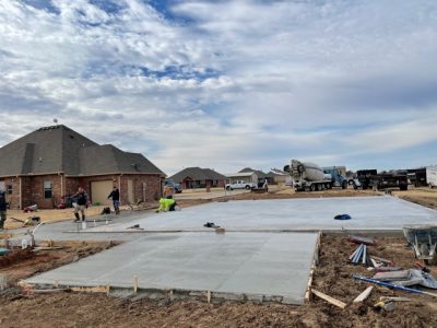 A concrete slab is being poured in front of a residential house, showcasing construction progress.