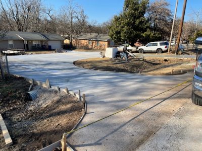 A construction crew is building a new driveway in a residential neighborhood, surrounded by houses and trees.
