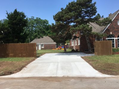 A driveway bordered by a fence, with a tree standing in the front yard, creating a welcoming residential scene.