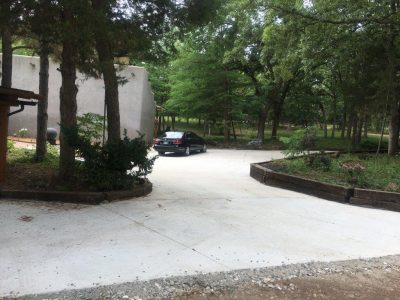 A driveway featuring a car parked centrally, surrounded by grass and trees.