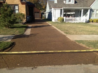A worker paves a new sidewalk in front of a residential house, with tools and materials visible nearby.