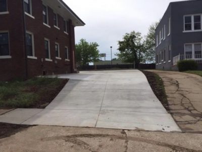 A concrete driveway is under construction in front of a residential house, with tools and materials visible.