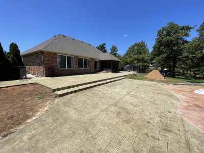 A concrete patio featuring a swimming pool adjacent to a house, showcasing a relaxing outdoor space.