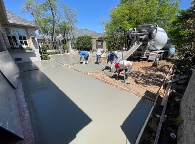  Concrete being poured in a backyard, with workers and equipment surrounding the area.
