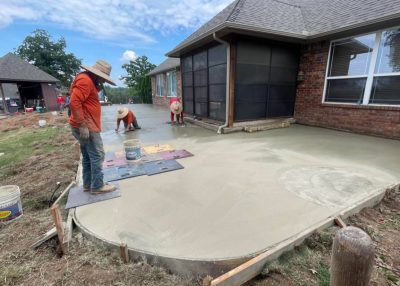 Concrete patio construction underway in Oklahoma, showcasing workers pouring and leveling fresh concrete on a sunny day.