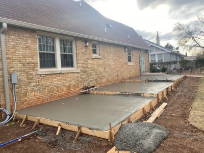 Fresh concrete is being poured in the backyard of a residential home, ready for a new patio or walkway installation.